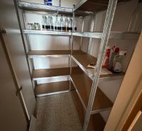 A pantry in a 2-room apartment with a storage rack and plastic bottles.