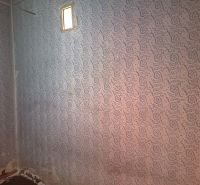 A wall with wallpaper in a family house with a small window.