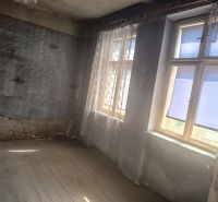Interior of a family house with wooden flooring, unrenovated walls, and windows with curtains.