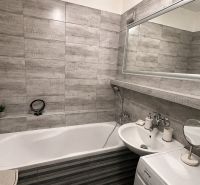 A bathroom with a bathtub, sink, and washing machine in a 3-room apartment. Gray tiles dominate the space.