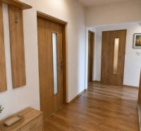 A hallway with a wooden decor floor, a mirror, and wooden furniture in a 3-room apartment.