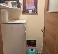 A small room with shelves, a refrigerator, a window, and cleaning equipment in the cottage.