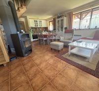Interior of a cabin with a staircase, seating area, fireplace, kitchen, and wooden decor flooring.