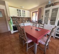 A kitchen in a cottage with white furniture, a dining table, and a terracotta floor.