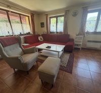 The interior of a cabin with a comfortable armchair, a red sofa, and a floor with a brick appearance.