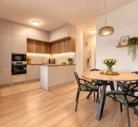 A kitchen with built-in appliances and a dining table in a 4-room apartment, with a wooden decor floor.