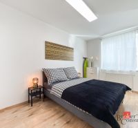 A bedroom with a bed, a nightstand, and a wooden decor floor in a studio apartment.
