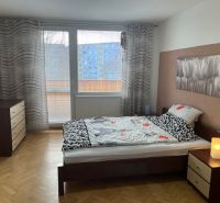 A bedroom in a three-room apartment with a wooden decor floor and balcony doors.