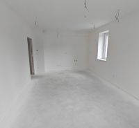A spacious room in a 2-room apartment with white walls and a large window.