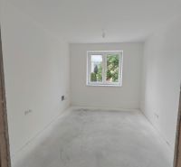 An empty room with white walls and a window in a 2-room apartment without flooring.