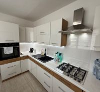 A kitchen in a 3-room apartment with white cabinets and appliances, and a wooden decor floor.