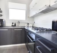 A kitchen with a stove, microwave, and coffee maker in a 3-room apartment, with a wooden decor floor.