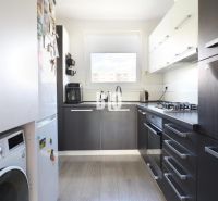 A kitchen with a washing machine and appliances in a 3-room apartment, floor with wood decor.