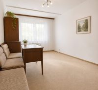 A room in a 3-room apartment with a sofa, a table, and carpeted flooring.