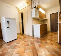 A kitchen in a 3-room apartment with wood-patterned tiles, cabinets, and a refrigerator.