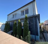 A family house in Komárno with a modern facade and a row of cypress trees in front of the entrance.