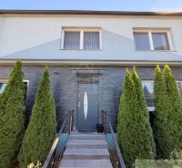 A family house in Komárno with a gray facade and thuja trees in front of the entrance.