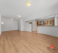 A spacious living area with a kitchenette and a wooden decor floor in a 2-room apartment.