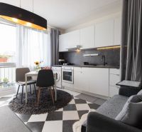 A kitchen in a 2-room apartment with a dining table, curtains, and black and white tiles.