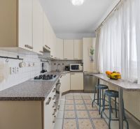 A kitchen in a 2-room apartment with a counter, chairs, and appliances, in light shades.