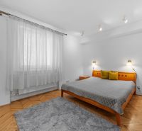 Bedroom with a bed, gray carpet, colorful pillows, wooden decor flooring in a 2-room apartment.