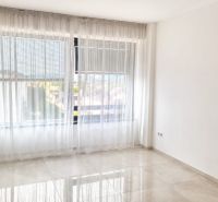 An empty room in a 2-room apartment with white curtains and tiled flooring.
