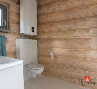 A bathroom with wooden walls, a sink, a toilet, and a boiler in a family house.