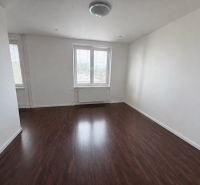 A bright room in a 2-room apartment with a wooden decor floor, one window with a radiator.