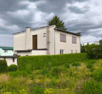 A family house in Nenince surrounded by greenery and a hedge under a cloudy sky.