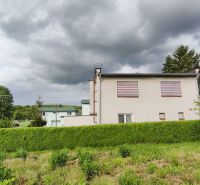 A family house in Nenince surrounded by dense greenery and trees under a cloudy sky.