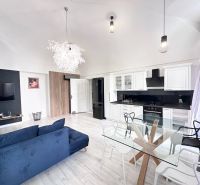 Living room in a three-room apartment with a sofa, kitchen unit, and glass table.