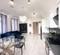 Living room with a corner sofa and kitchen in a 3-room apartment with a wooden decor floor.