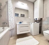 A bathroom in a 3-room apartment with a bathtub, washing machine, and a large mirror.