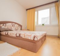 A bright bedroom with a bed, wooden floor decor, and yellow curtains in a three-room apartment.