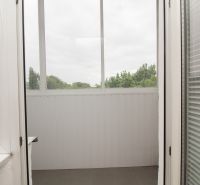 A bright loggia with blinds in a 3-room apartment with a view of greenery.