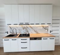 Kitchen unit in a one-room apartment with white cabinets and a wooden decor floor.