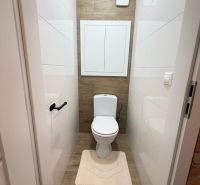 Bathroom with toilet, white tiles, and a floor with a wood decor in a studio apartment.