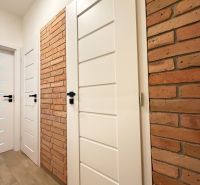 White door and brick wall in a studio apartment with wood-patterned flooring.