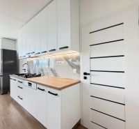 A kitchen in a studio apartment with white cabinets, marble tiles, and a wood-patterned floor.