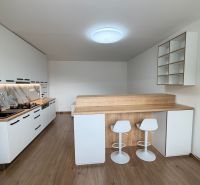A kitchen in a studio apartment with a wood-patterned floor, white furniture, bar stools.