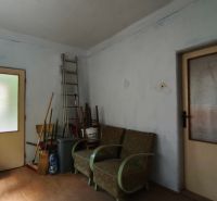 A room in a family house with armchairs, a ladder, and brooms on a wooden-decorated floor.
