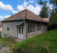 A family house in Olováry with a sloped roof, surrounded by a garden and green trees.