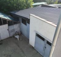 A family house in Nitra with a garage, a concrete yard, and greenery in the background.