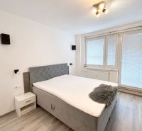 A bedroom with a double bed, wooden decor flooring, and a window in a three-room apartment.
