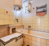 A bathroom in a family house with tiles and a bathtub, equipped with an old boiler.