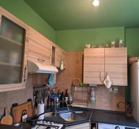 A kitchen in a 2-room apartment with wooden cabinets and a green wall.