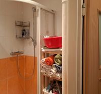 Shower corner with orange tiles and a shelf with towels in a 2-room apartment.