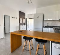 A kitchen in a studio apartment with a bar counter, white kitchen cabinets, and appliances.