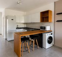 A kitchenette in a studio apartment with a bar counter, washing machine, and refrigerator.