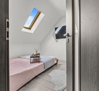 Attic bedroom with a window, bed, and wooden decor flooring in a family house.